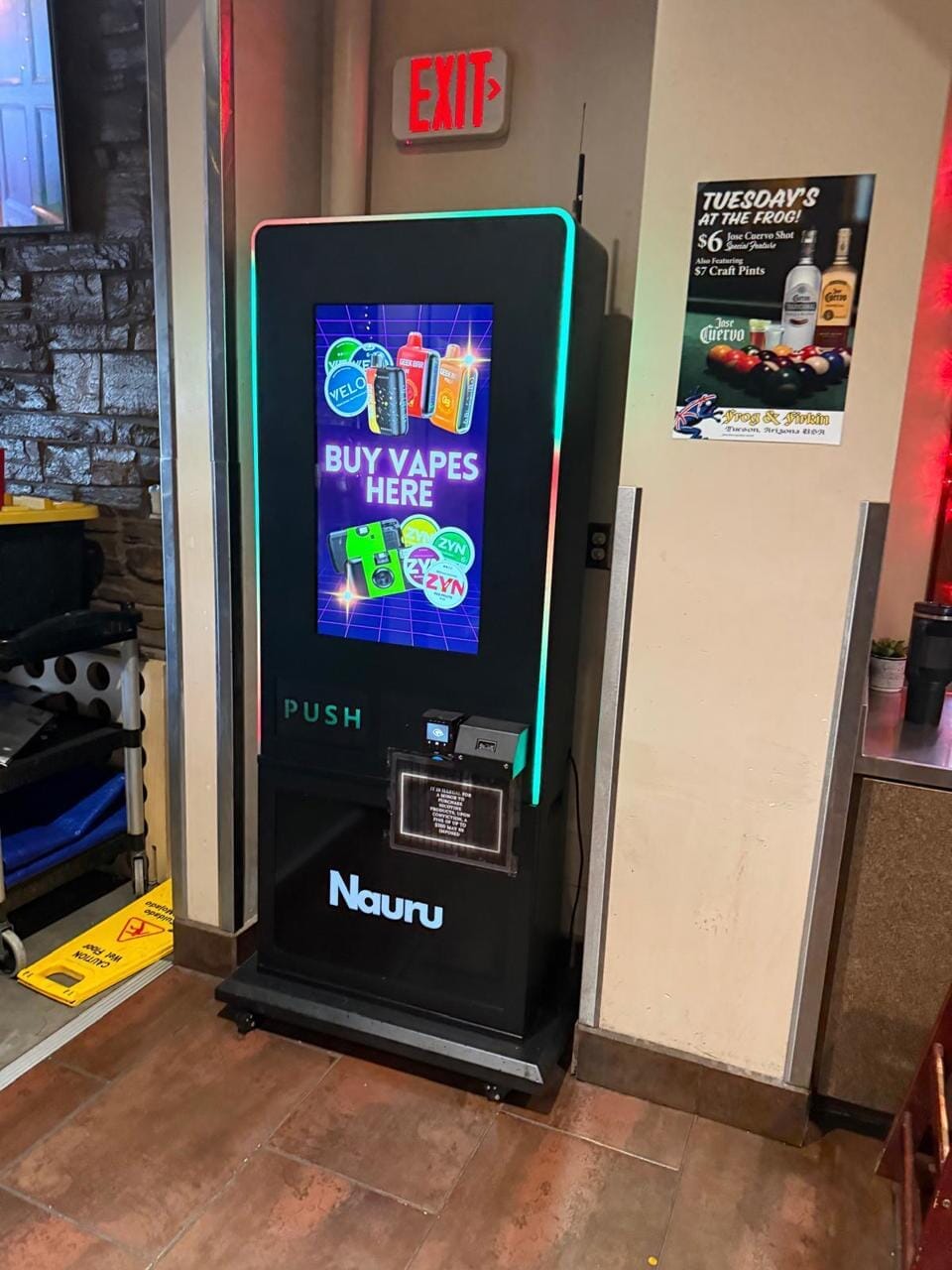 Nauru-branded VTM Vape machine inside a restaurant bar area with a digital 'Buy Vapes Here' display featuring ZYN, VELO, and Geek Bar products
